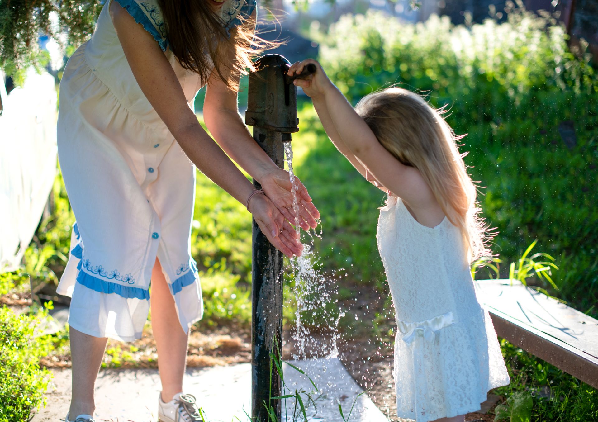 Mutter und Kind waschen sich im Garten die Hände mit Wasser aus einem erdtank mit regenwasser