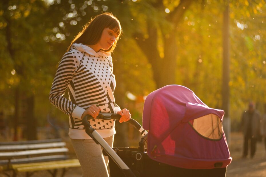 Junge Mutter spaziert mit Kinderwagen und lächelt.